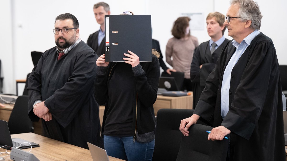 Die Angeklagte Lina E. steht im Oberlandesgericht Dresden im Verhandlungssaal und hält einen Aktenordner vor ihr Gesicht (Archivbild)