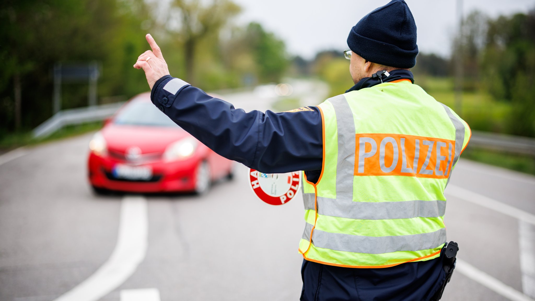 Ein Polizist winkt am 19.04.24 an einer Staatsstraße außerorts bei Wessobrunn (Bayern) ein Fahrzeug aus dem Verkehr (Symbolbild).