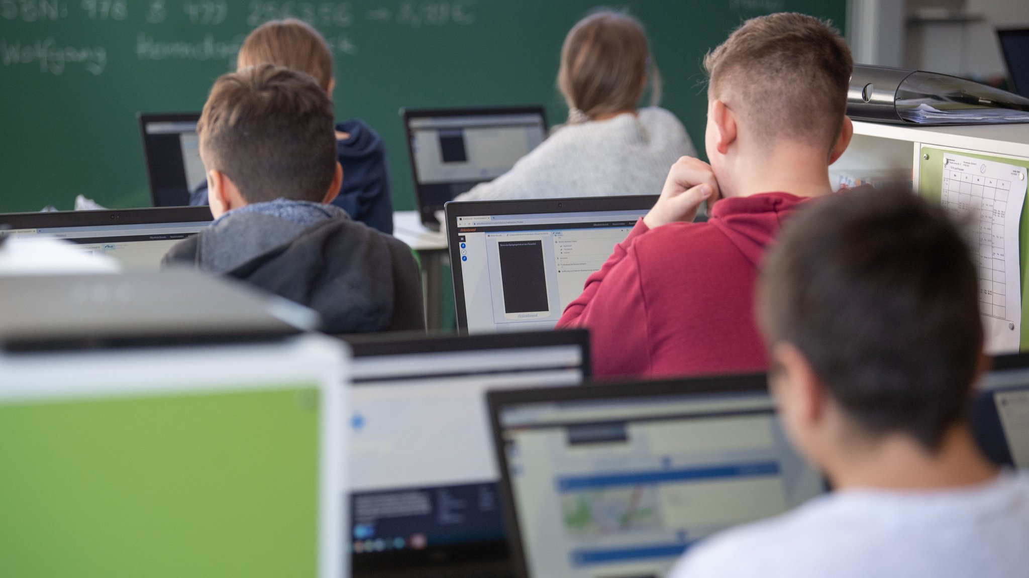 Schülerinnen und Schüler mit Notebooks im Klassenzimmer, von hinten gesehen