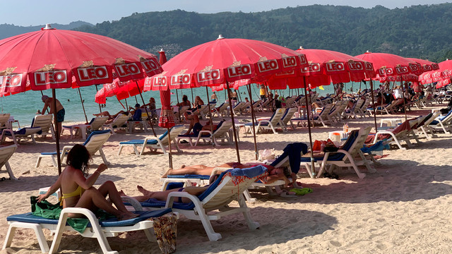 Touristen liegen unter Sonnenschirmen am Patong Beach.