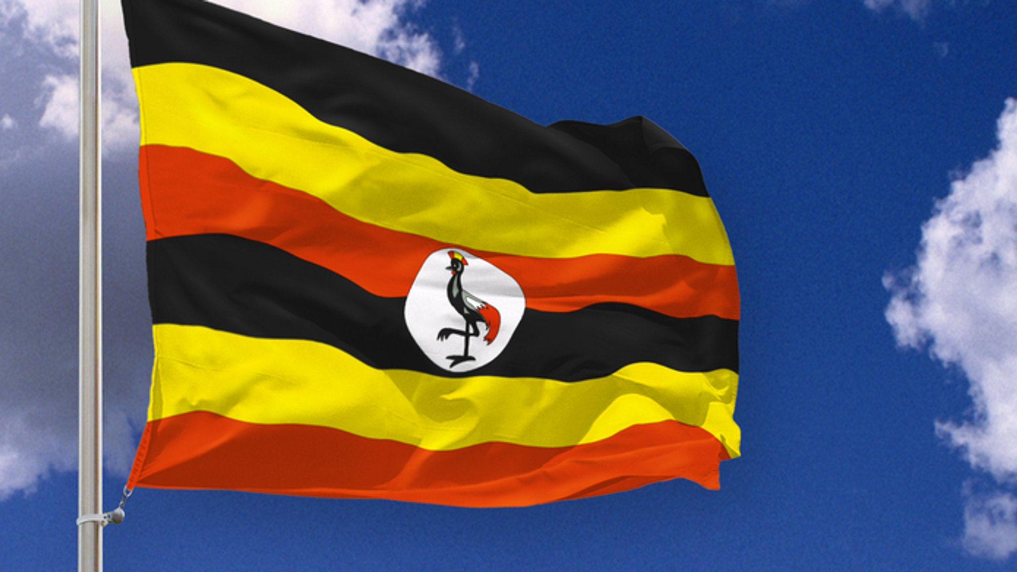 Flagge von Uganda weht im Wind vor blauem Himmel 