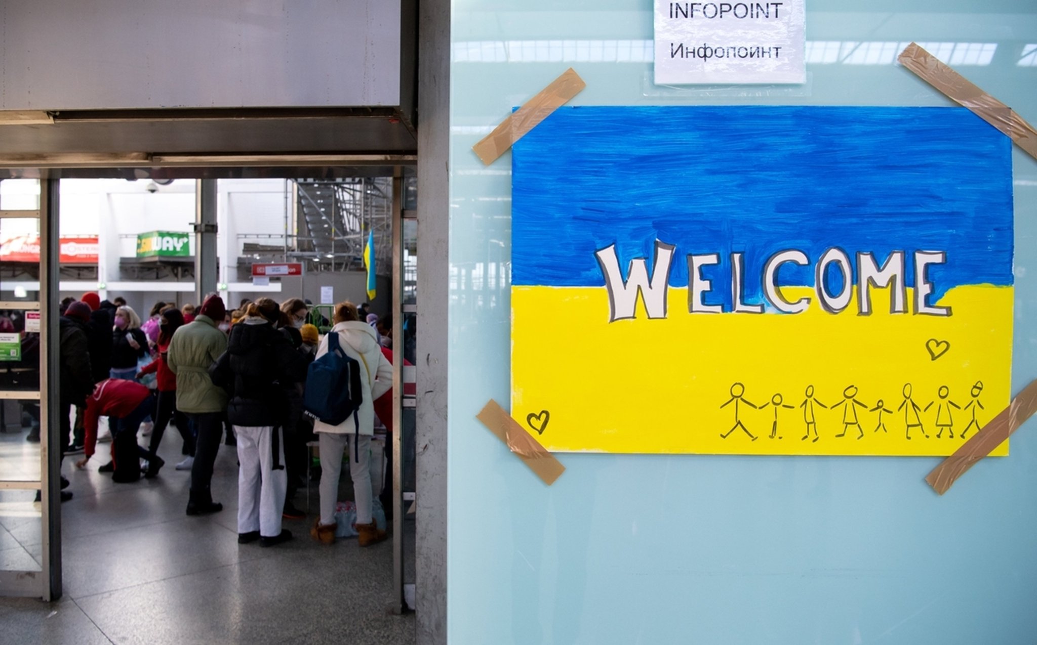 RCHIV - 09.03.2022, Bayern, München: Ein Schild in den Farben der Ukraine mit der Aufschrift "Welcome" ist am Hauptbahnhof zu sehen. Im Hintergrund werden Flüchtlinge aus der Ukraine nach ihrer Ankunft von Mitarbeitern der Caritas und freiwilligen Helfern empfangen.