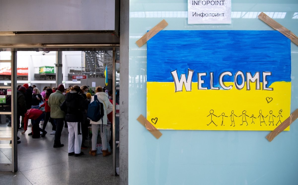 RCHIV - 09.03.2022, Bayern, München: Ein Schild in den Farben der Ukraine mit der Aufschrift "Welcome" ist am Hauptbahnhof zu sehen. Im Hintergrund werden Flüchtlinge aus der Ukraine nach ihrer Ankunft von Mitarbeitern der Caritas und freiwilligen Helfern empfangen.
