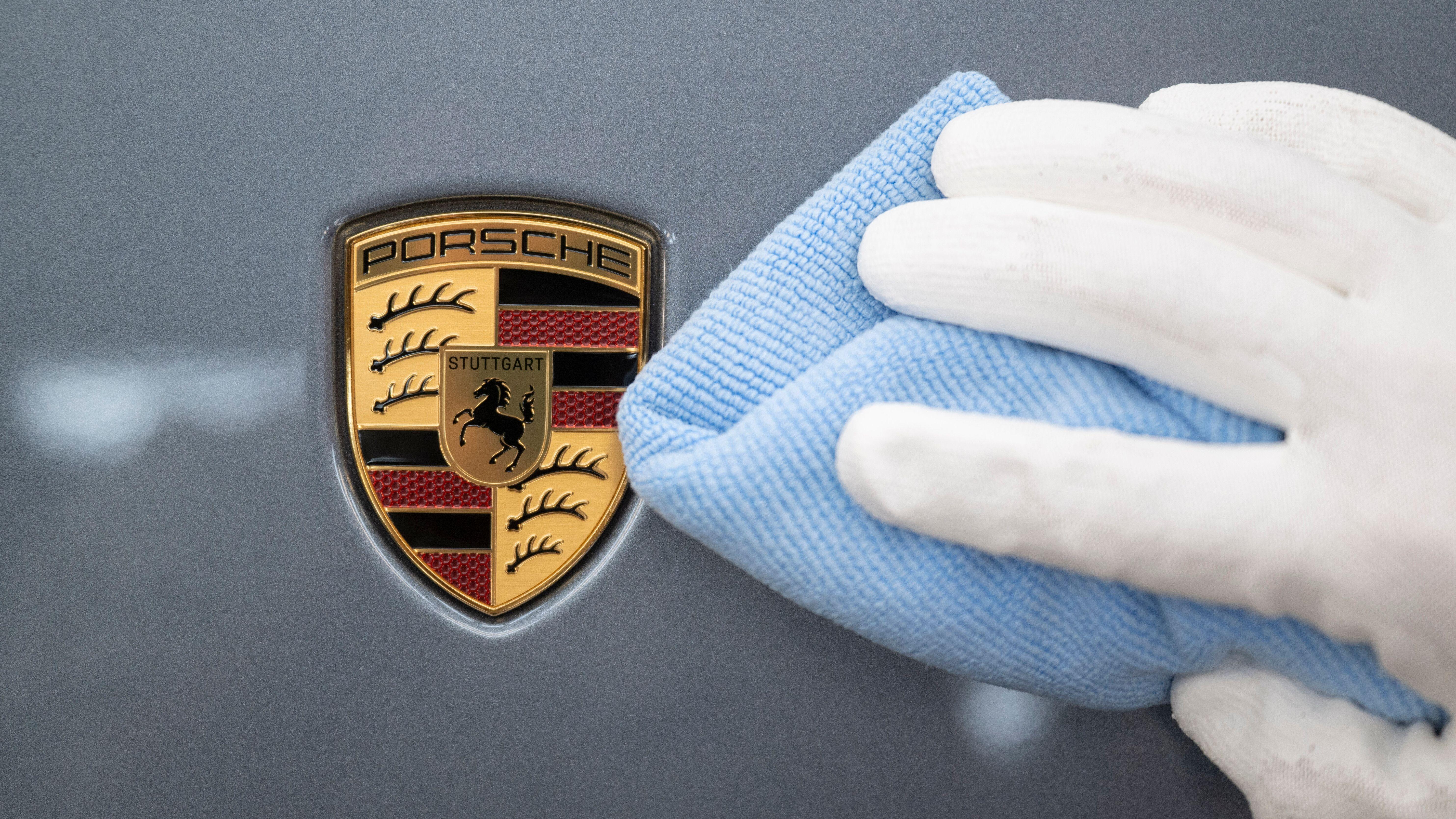 Ein Mitarbeiter der Porsche AG poliert im Stammwerk in Zuffenhausen ein Fahrzeug. Man sieht das Porsche-Emblem.