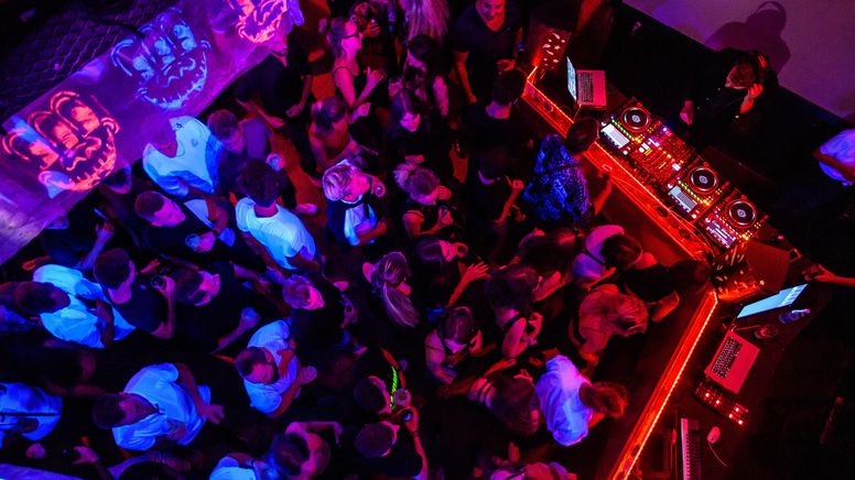 Vogelperspektive: Man sieht Feiernde auf engem Raum, rotes Licht, DJ-Pult, Getränke in vielen Händen. | Bild:picture alliance/dpa | Matthias Balk