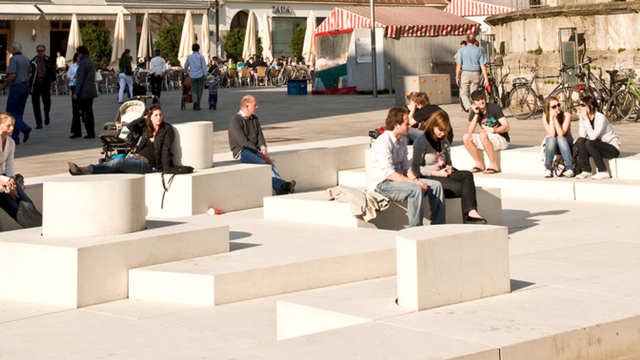 Menschen sitzen auf dem begehbaren Denkmal des israelischen Künstlers Dani Karavan auf dem Neupfarrplatz in Regensburg