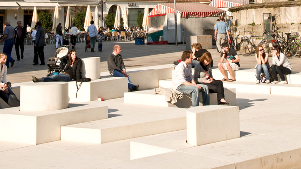 Menschen sitzen auf dem begehbaren Denkmal des israelischen Künstlers Dani Karavan auf dem Neupfarrplatz in Regensburg