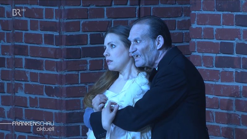 Graf Dracula mit spitzen Zähnen umarmt eine junge Dame von hinten.