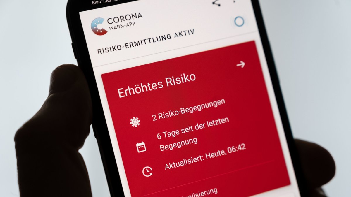 Ein Mann hält ein Smartphone in der Hand, auf dem die Corona-Warn-App ein erhöhtes Risiko anzeigt