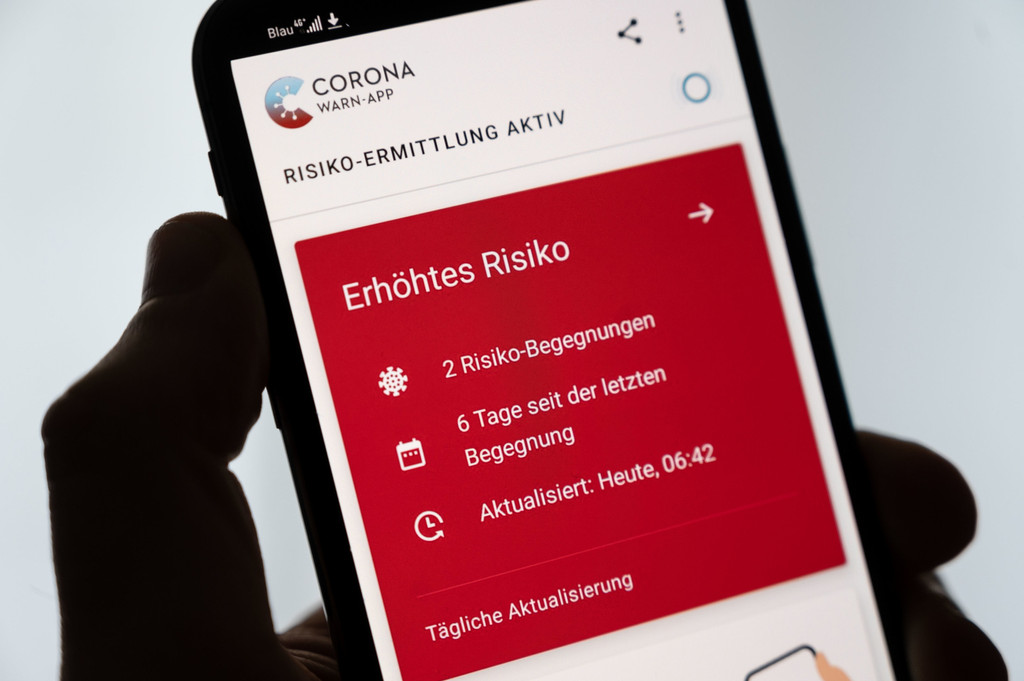 Ein Mann hält ein Smartphone in der Hand, auf dem die Corona-Warn-App ein erhöhtes Risiko anzeigt