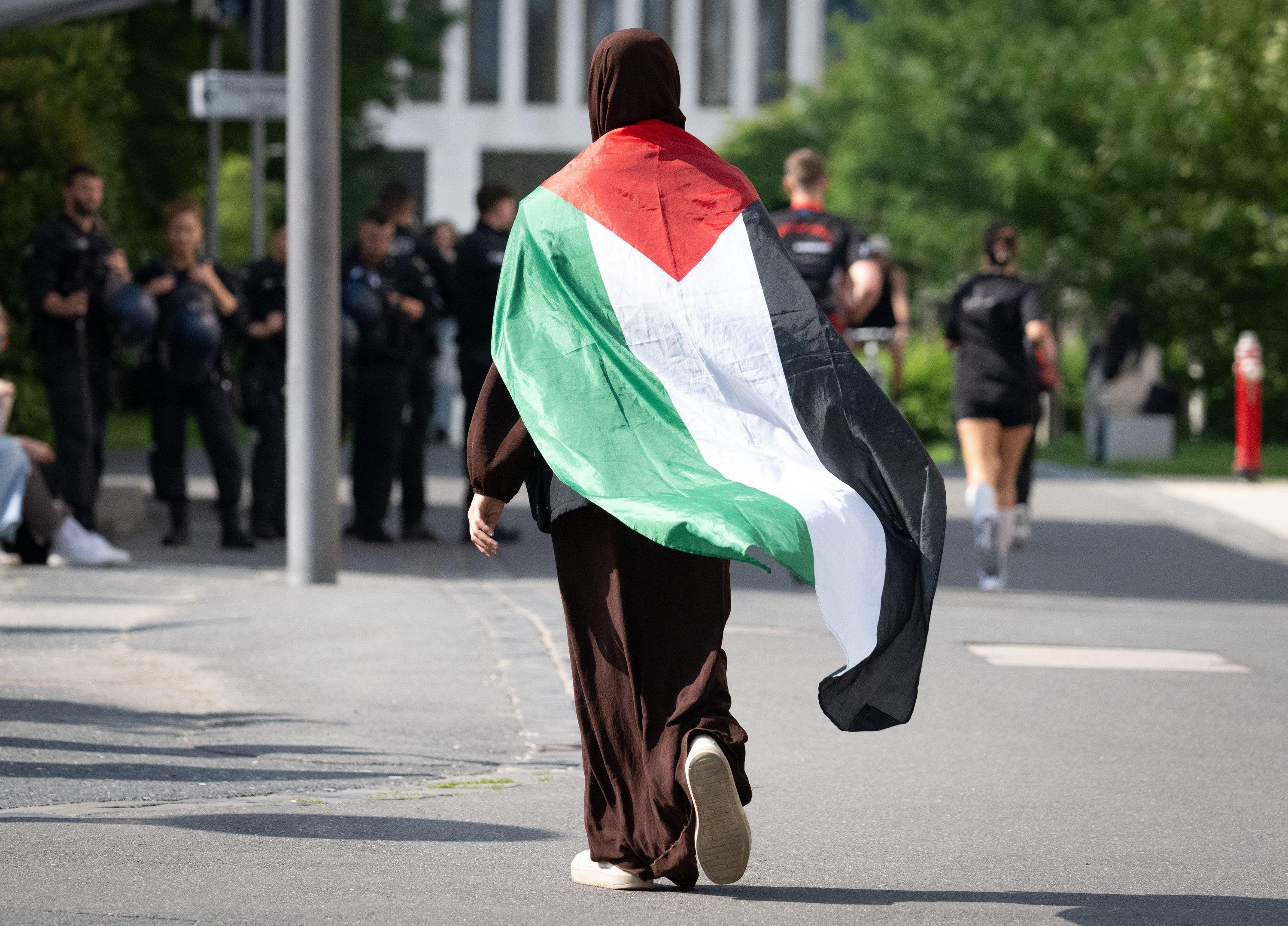 Eine Frau geht in Frankfurt am Main mit einer umgehängten Palästina-Fahne zu einer Demonstration (Archivbild)