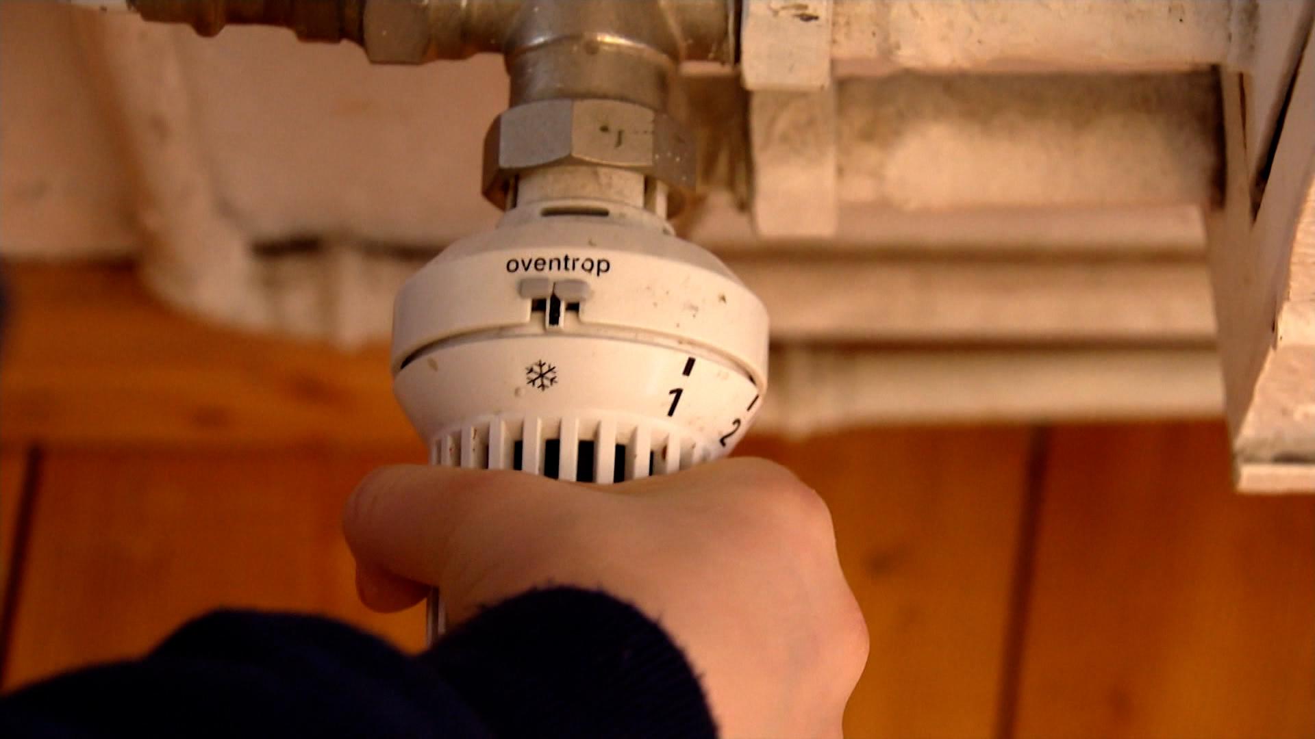 Eine Person dreht am Thermostat einer Heizung.