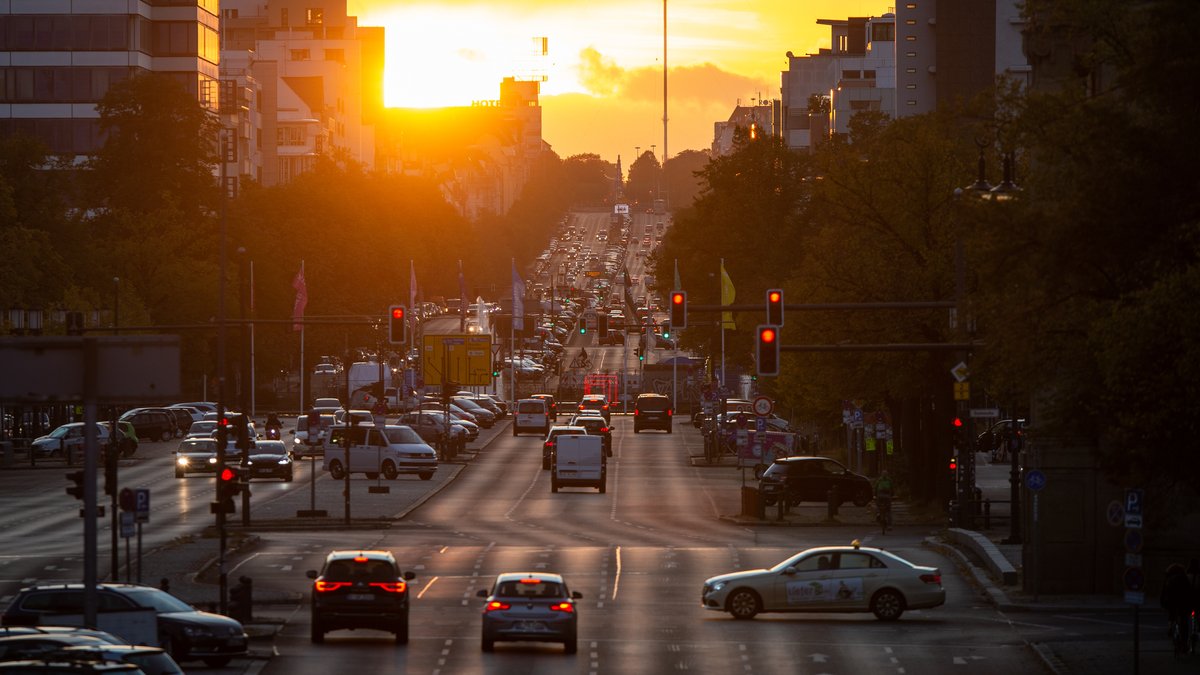 Autos fahren auf der Straße des 17. Juni, während im Hintergrund die Sonne untergeht.