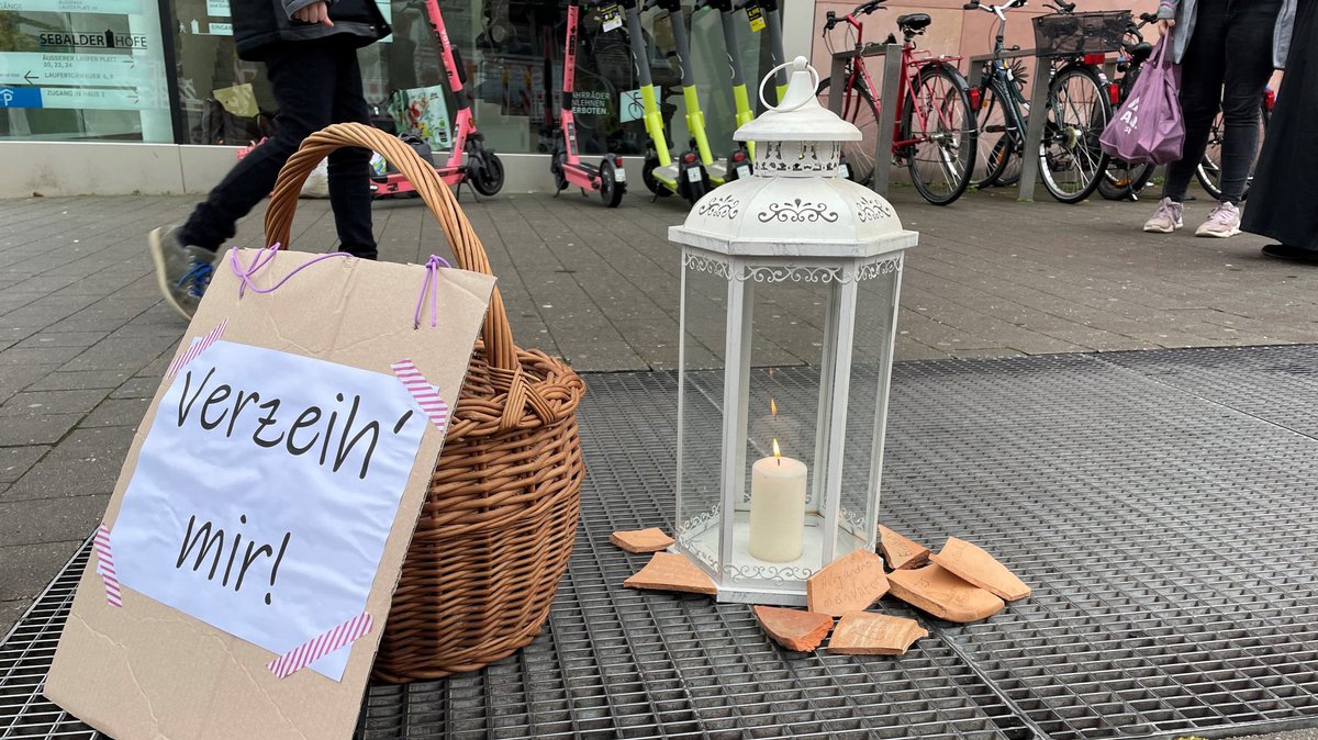 Eine Laterne mit brennender Kerze, ein Korb und ein Plakat mit der Aufschrift "verzeih' mir!" auf einem Lüftungsschacht.