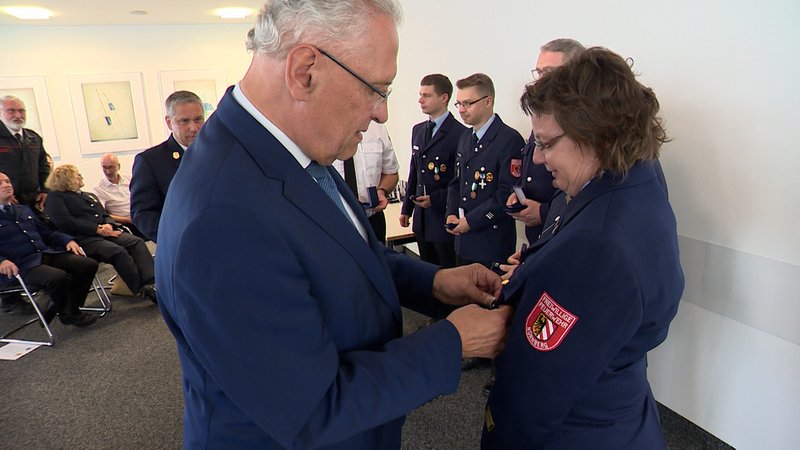 Innenminister Joachim Herrmann (CSU) heftet einer Feuerwehrfrau eine Auszeichnung an.