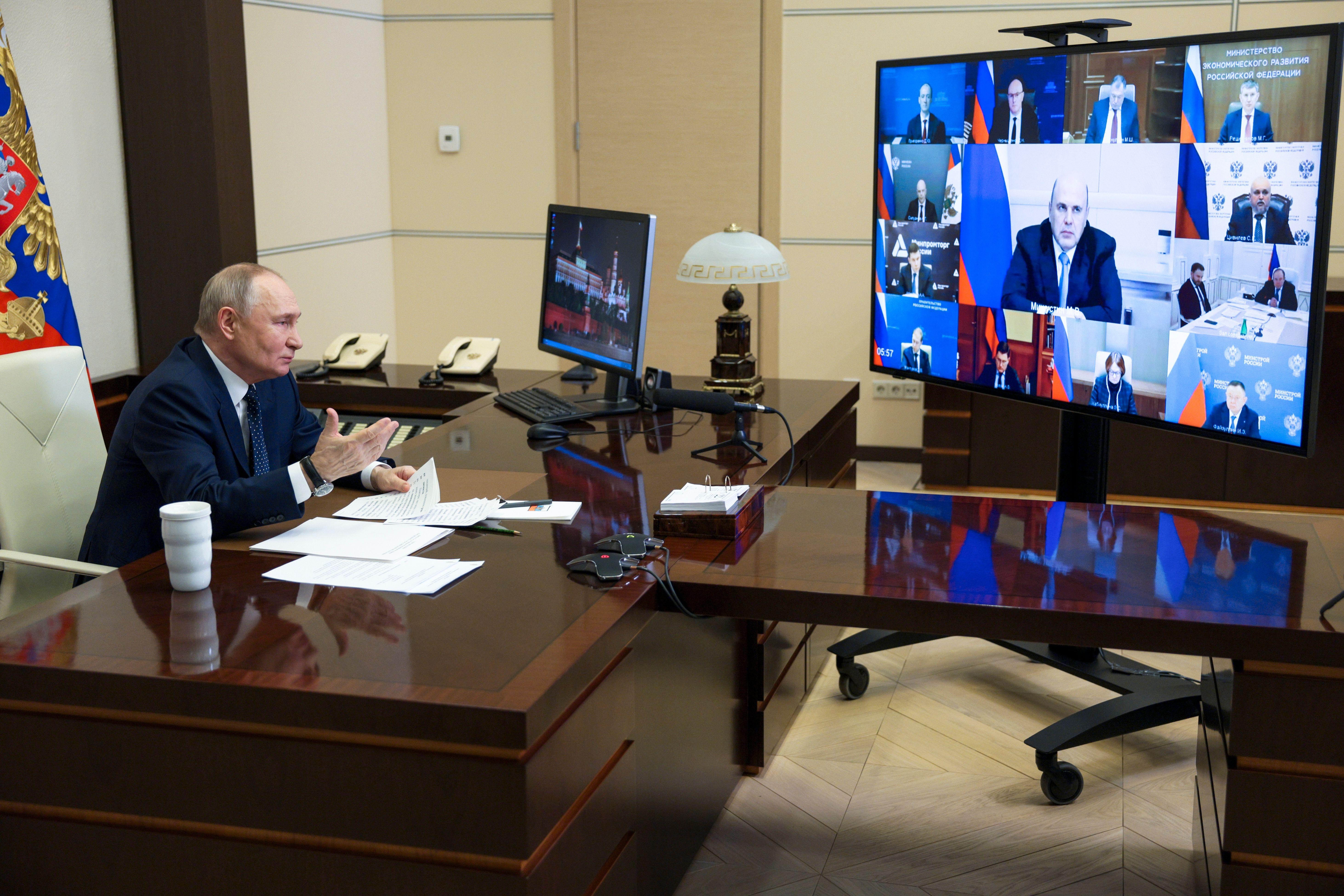 Der russische Präsident sitzt am Schreibtisch vor einem Videobildschirm