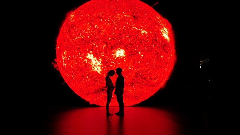 Ein Paar steht vor einem rotglühenden Kreis, der aussieht wie ein Sonnenball (Filmszene aus "Ema")