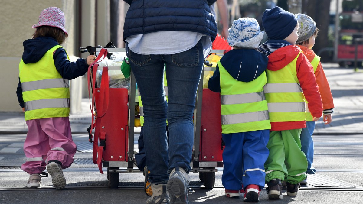 Ein Betreuerin läuft mit mehreren Kleinkindern über einen Bürgersteig.