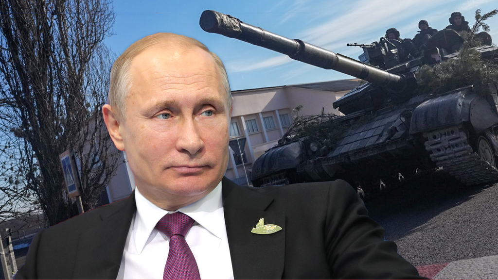 Ein Mann mit Anzug und Krawatte, es ist der russische Präsident Wladimir Putin. Hinter ihm ist ein Panzer zu sehen.