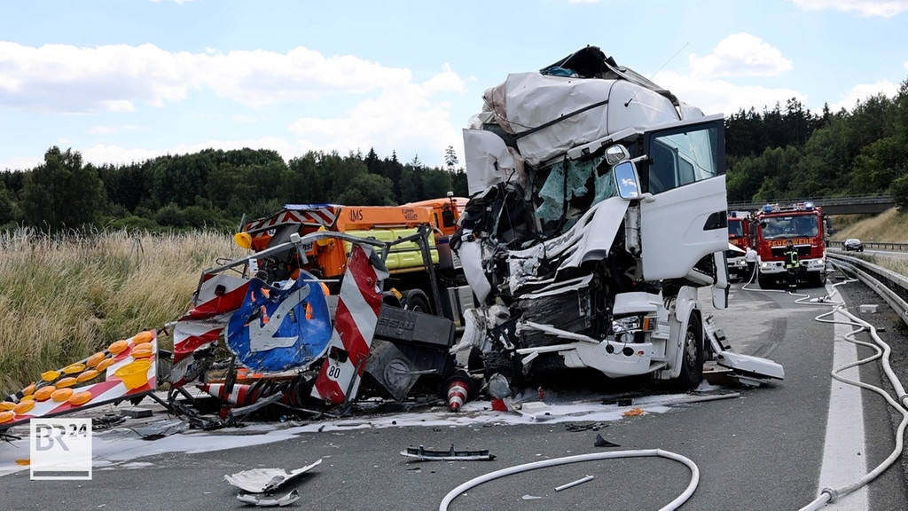 Das zerbeulte Führerhaus eines Lastwagens steht neben einem Warnleitanhänger, im Hintergrund stehen Feuerwehrautos. Unfall auf der A93 bei Selb