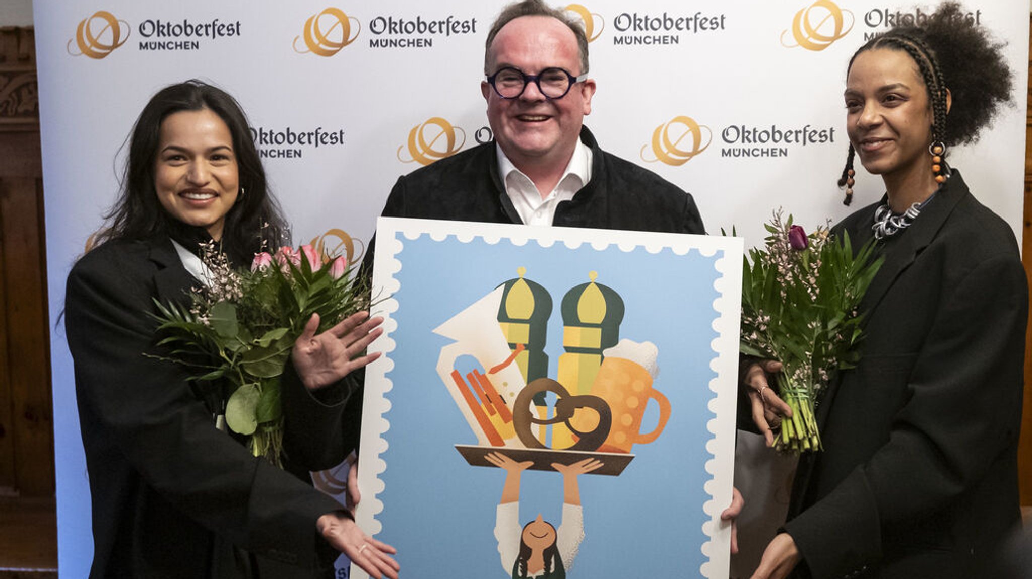 07.02.2025, Bayern, München: Wiesnchef Clemens Baumgärtner (M.) präsentiert mit den Künstlerinnen Amiera Harithas (l.) und Dianah-Charles Francis das offizielle Motiv zum Oktoberfest 2025. Das Motiv wird auf dem offiziellen Plakat für die Wiesn werben sowie auf einer Reihe Produkte zu sehen sein. Foto: Lukas Barth/dpa +++ dpa-Bildfunk +++