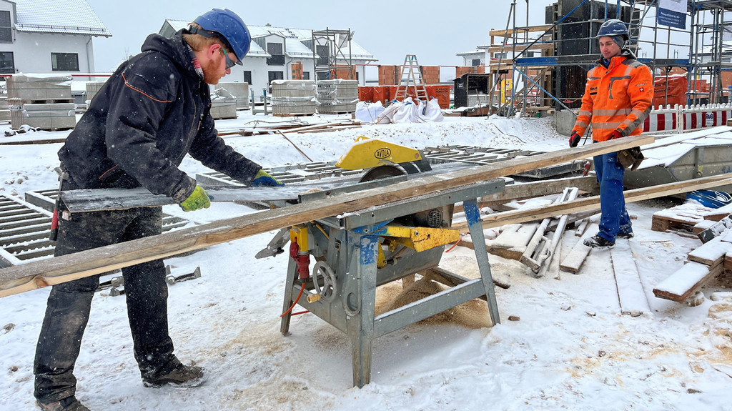 Zwei Bauarbeiter sägen Holz auf einer Baustelle.