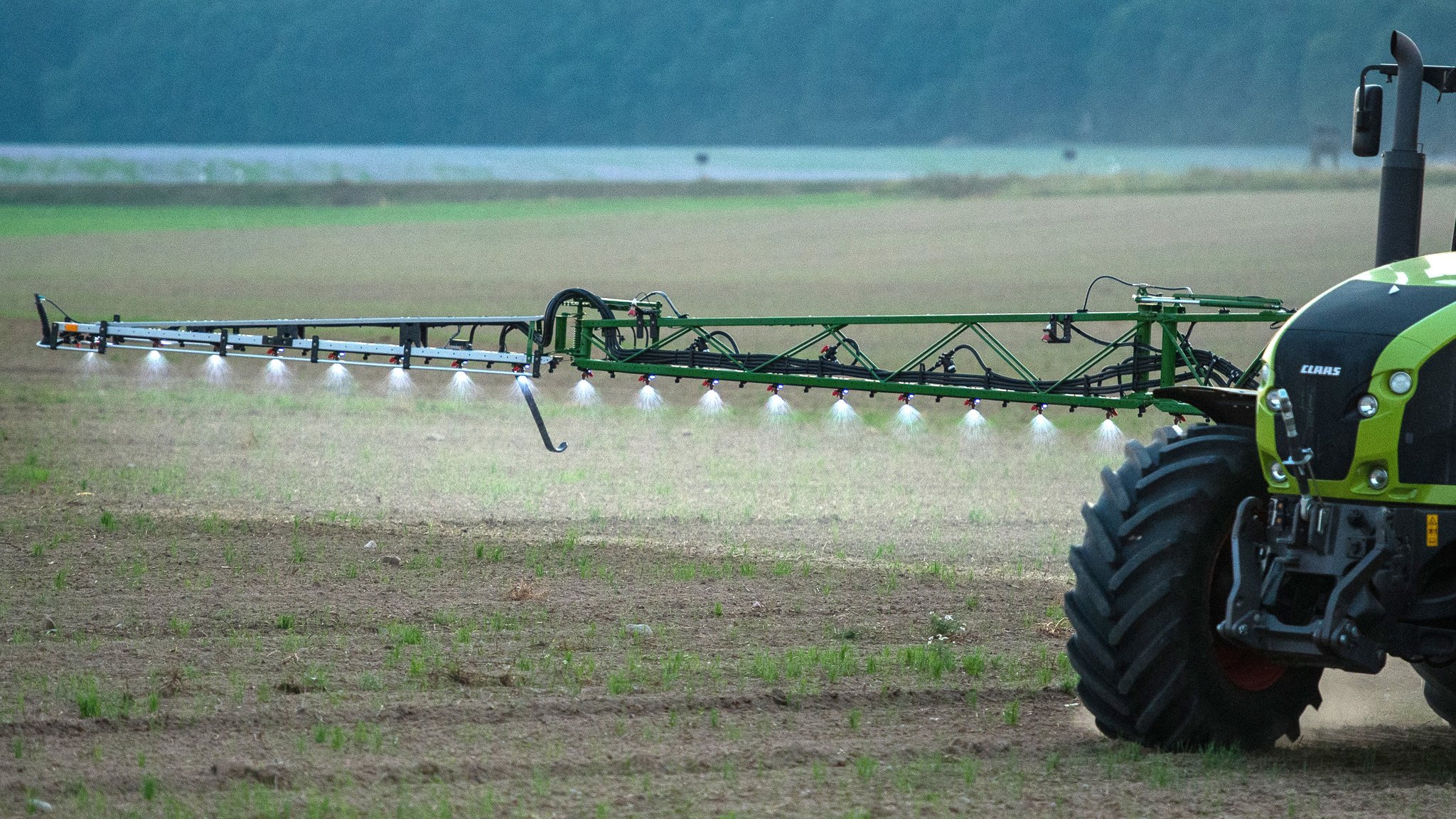 Ein Landwirt fährt abends mit einer Pestizid- und Düngerspritze über ein Feld