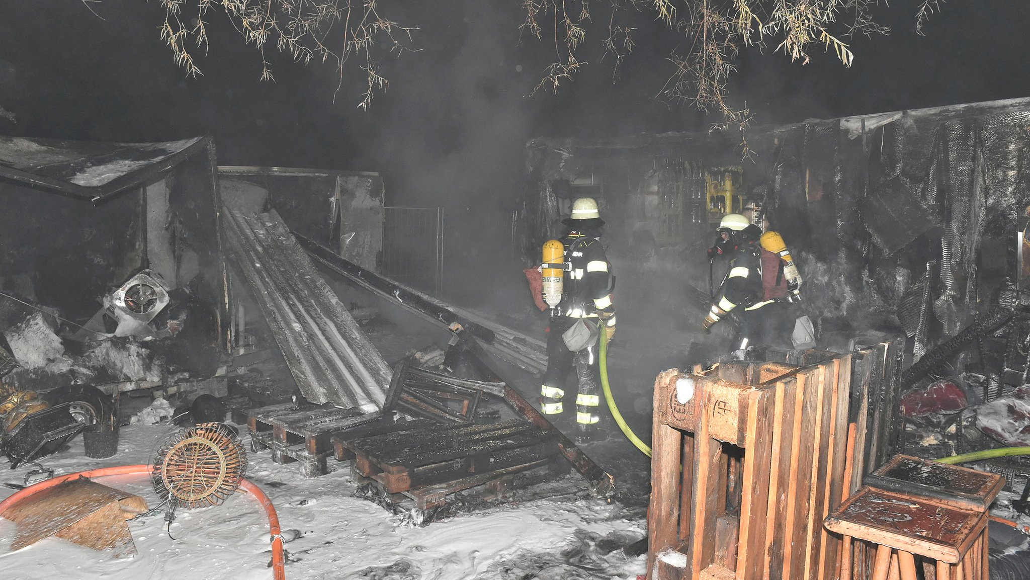 Feuerwehrmänner stehen zwischen Rauchschwaden und niedergebrannten Bars.