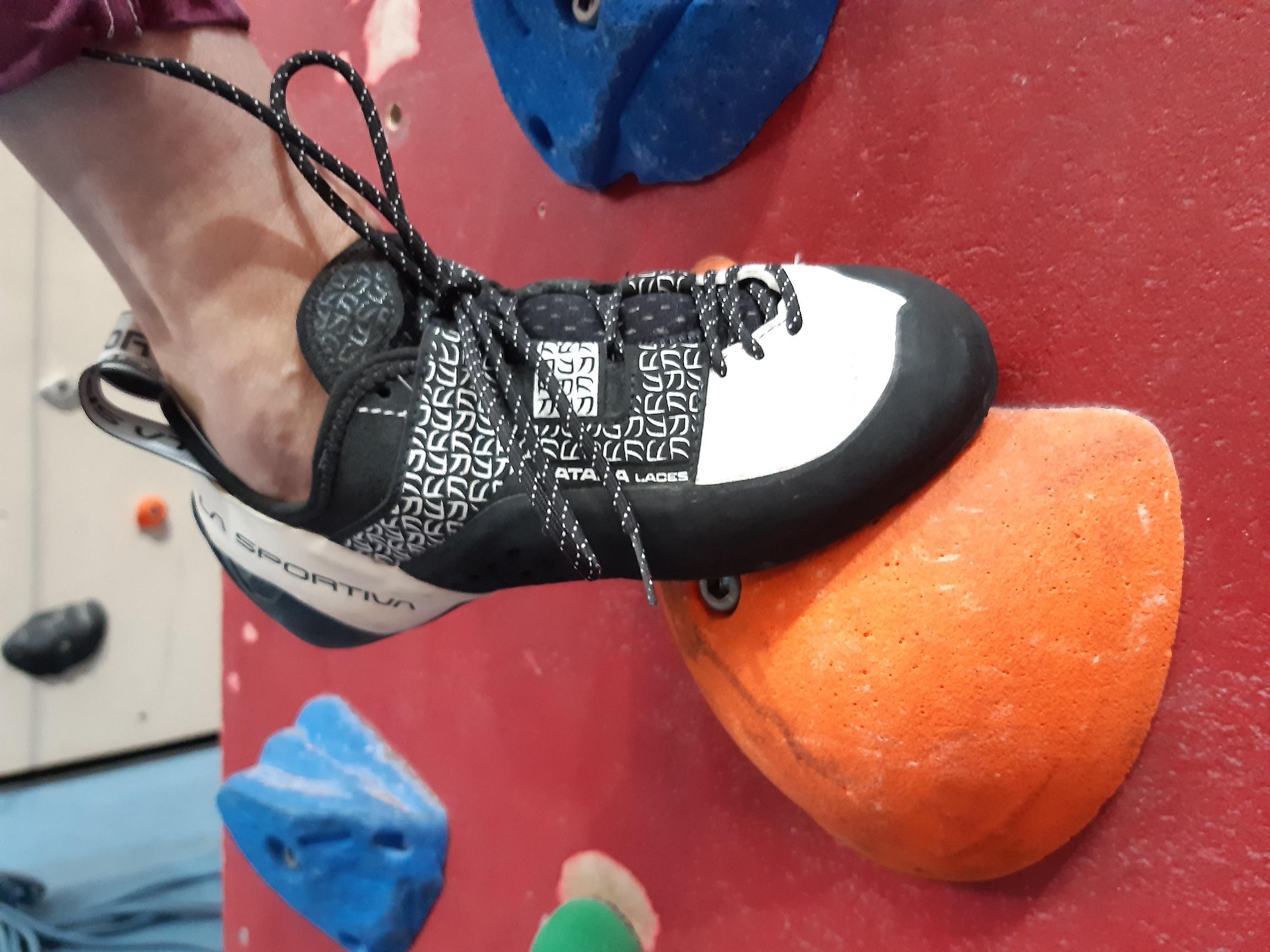 Schwarzweißer Kletterschuh einer Sportlerin, die in der Kletterhalle Weilheim auf einem organgefarbenen Tritt steht 