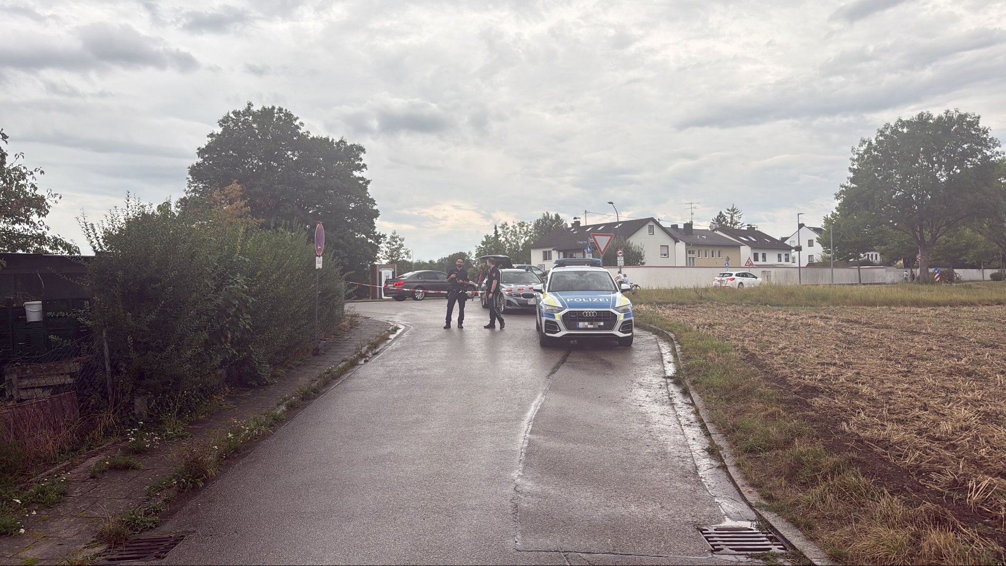 Ein Polizeiauto und Einsatzkräfte stehen auf einer Straße neben einem Feld.