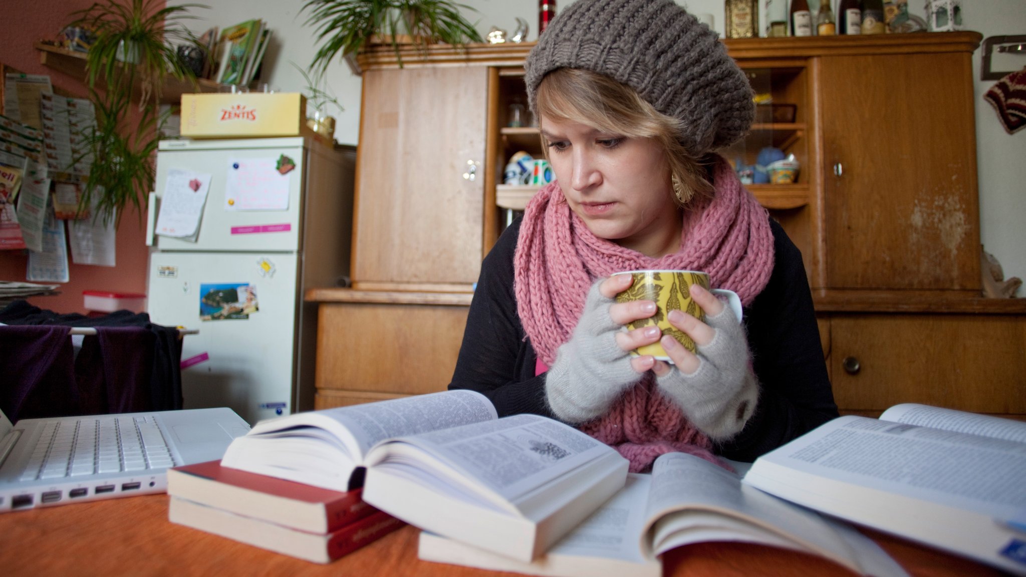 Studentin beim Lernen am Küchentisch mit Teetasse und Handschuhen