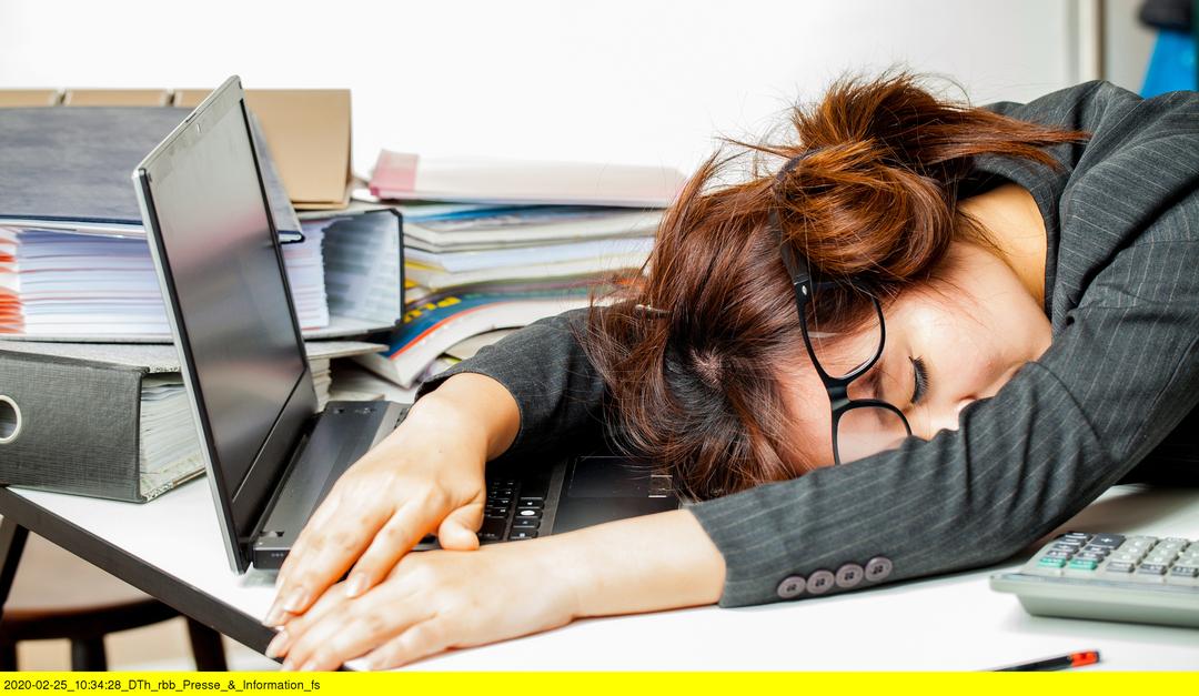 Arbeit bis zur Erschöpfung. Eine Frau liegt auf dem Schreibtisch.