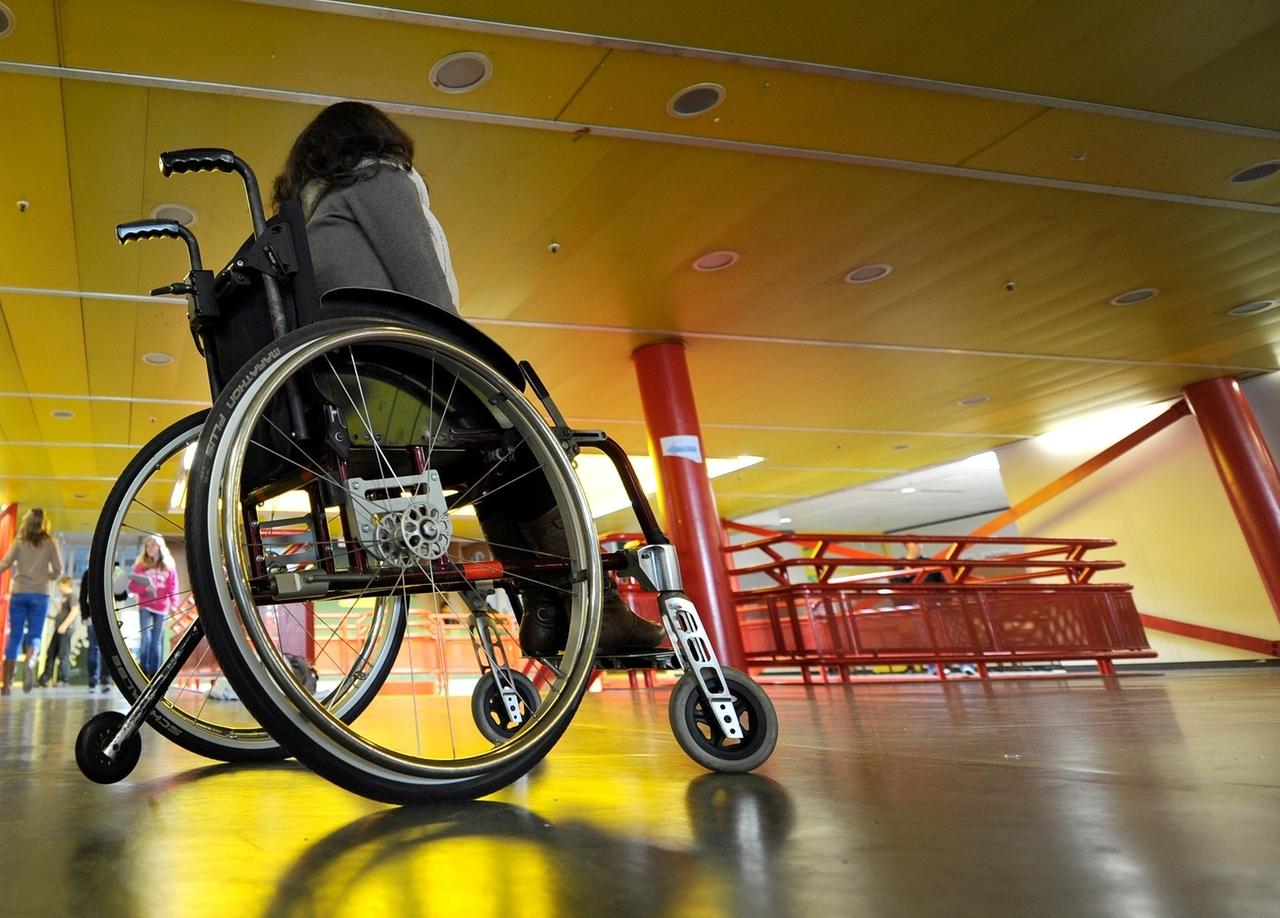 Eine Frau in einem Rollstuhl, von hinten und unten fotografiert. Ihr Gesicht ist nicht zu sehen.