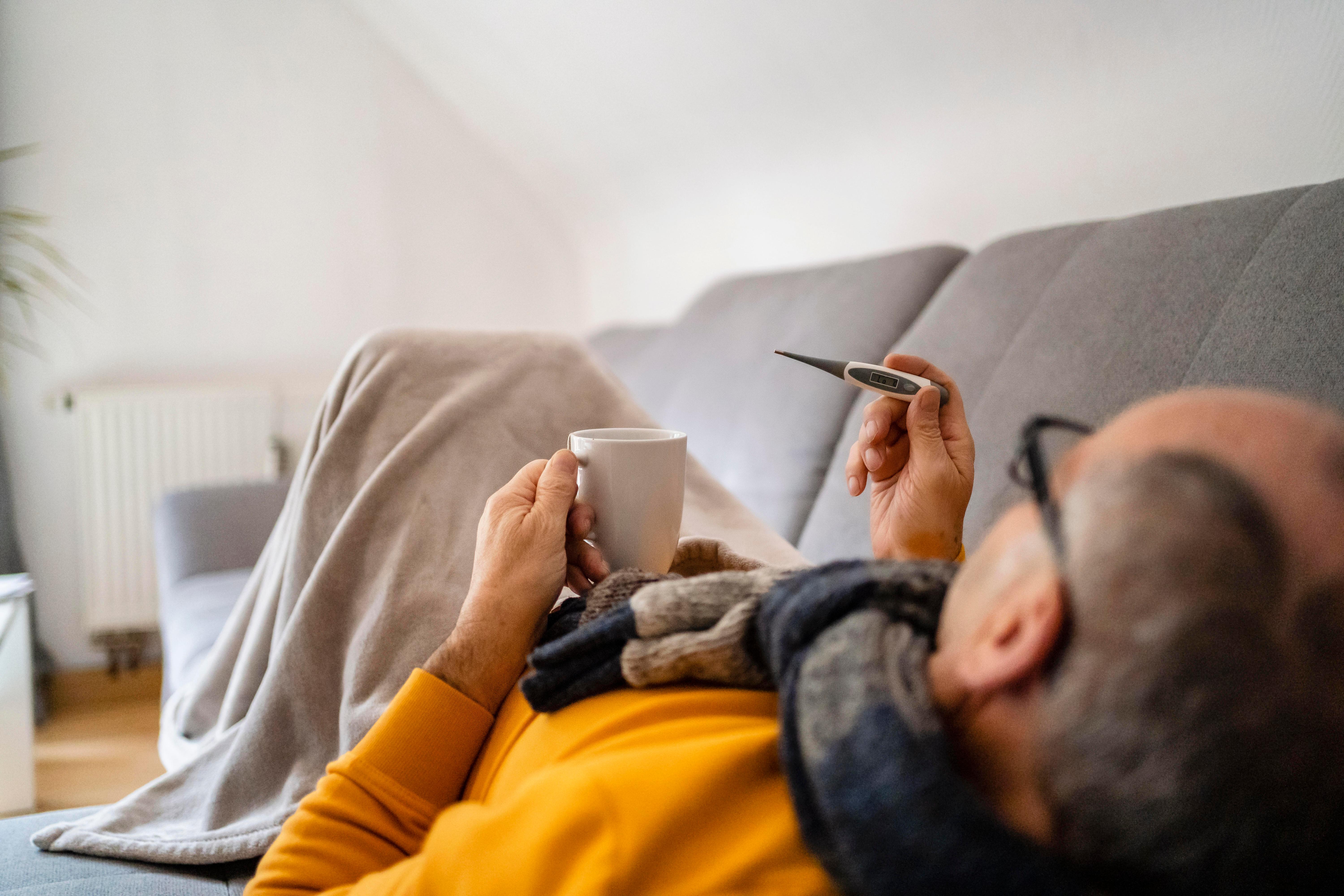 Symbolbild: Ein Mann liegt krank auf dem Sofa  