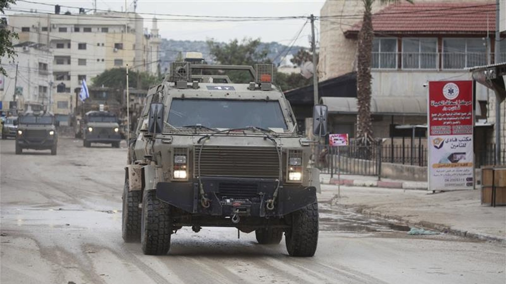 Ein israelisches Militärfahrzeug fährt auf einer Straße neben Schildern mit arabischer Aufschrift.