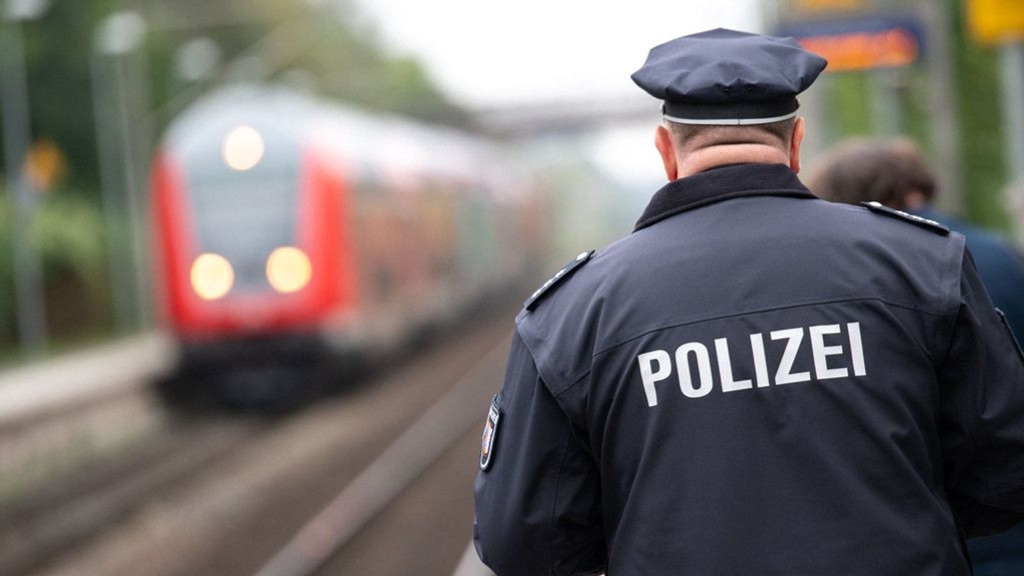 Polizist in blauer Uniform auf einem Bahnsteig von hinten.