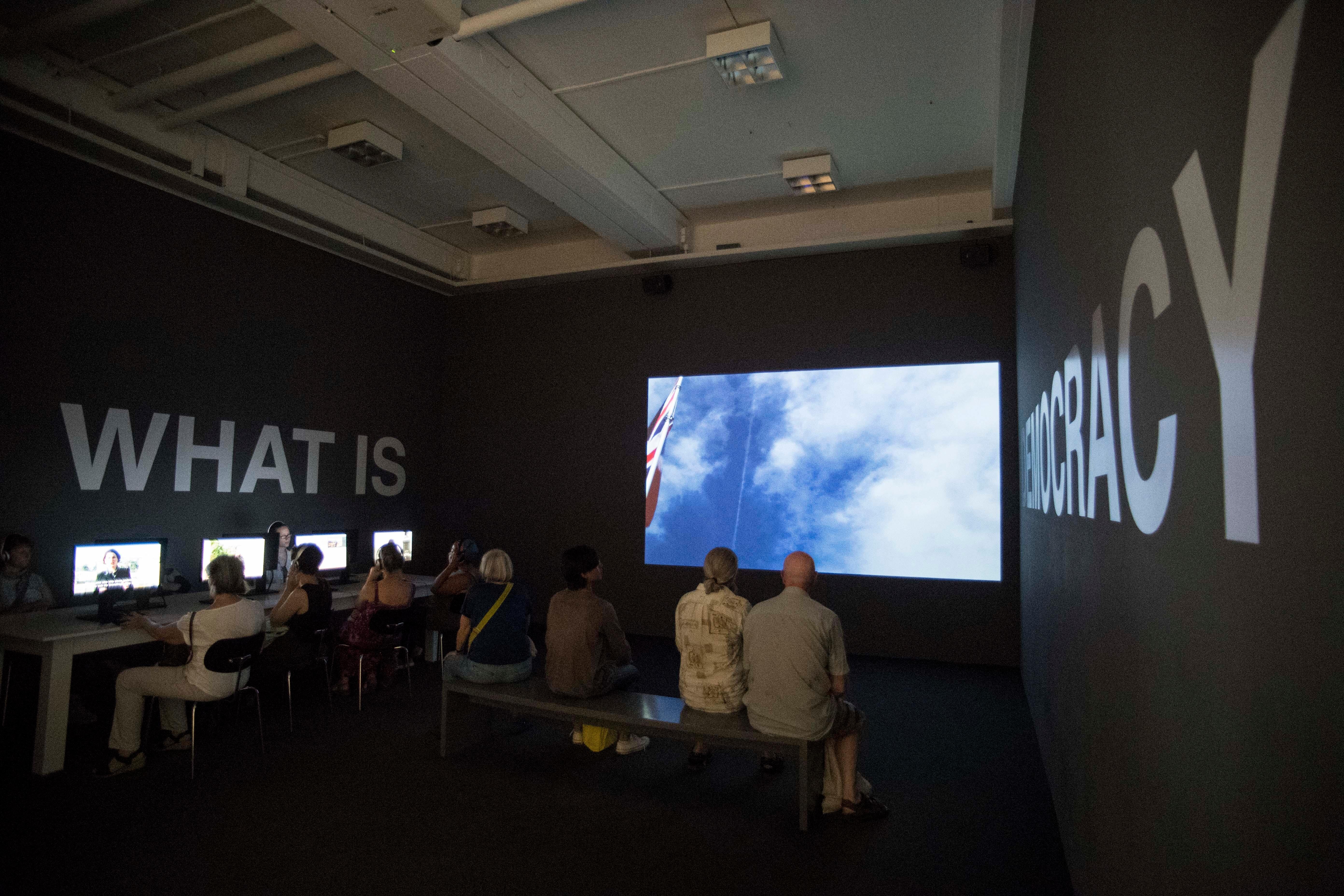 Videoinstallation von Oliver Ressler: Zuschauer sitzen vor Bildschirm  | Bild:Elmar Kremser/Sven Simon