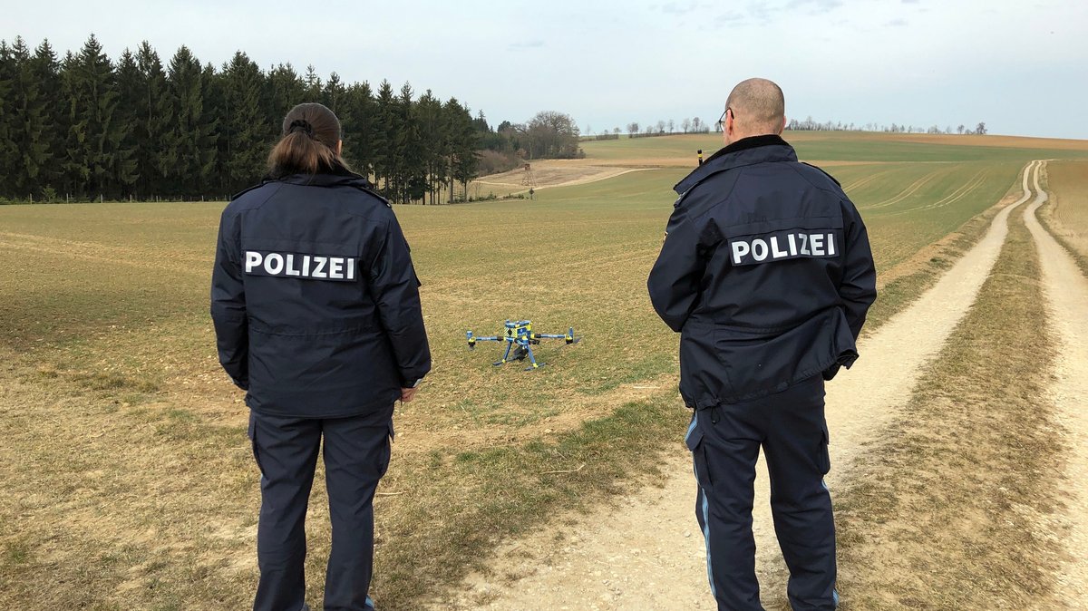 Polizisten stehen auf einem Feldweg vor einer Drohne. 