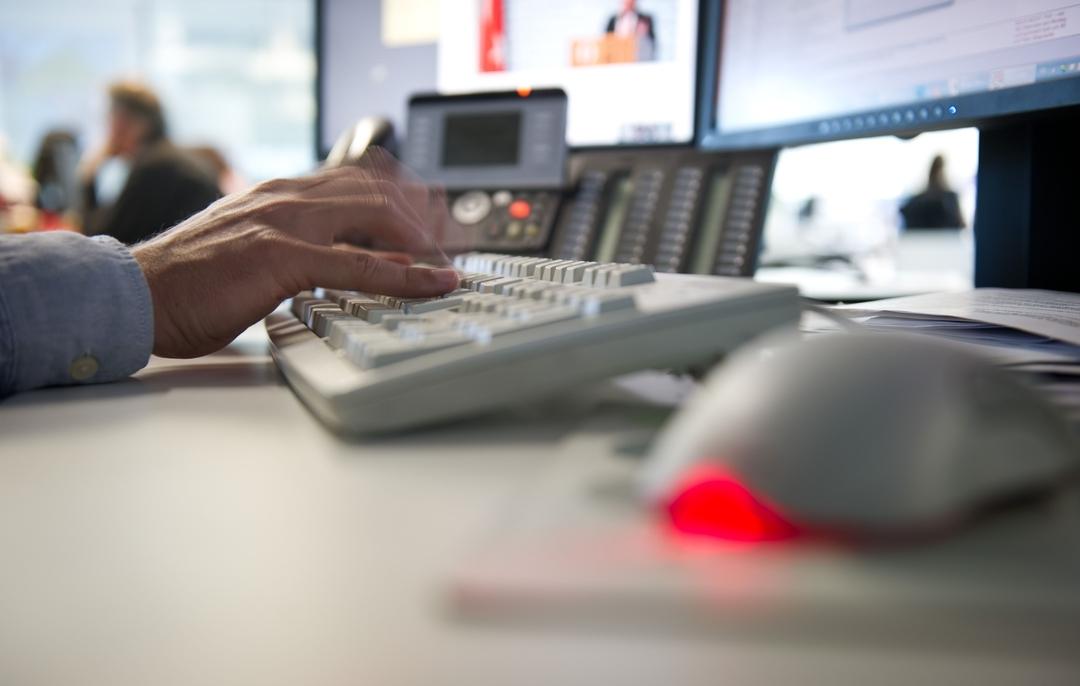 Foto eines Schreibtisches. Eine Computermaus und eine Tastatur, auf der getippt wird.