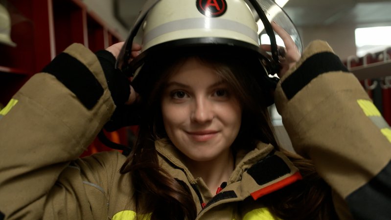 Eine Feuerwehrfrau setzt sich einen Helm auf. | Bild: BR Eine Feuerwehrfrau setzt sich einen Helm auf.