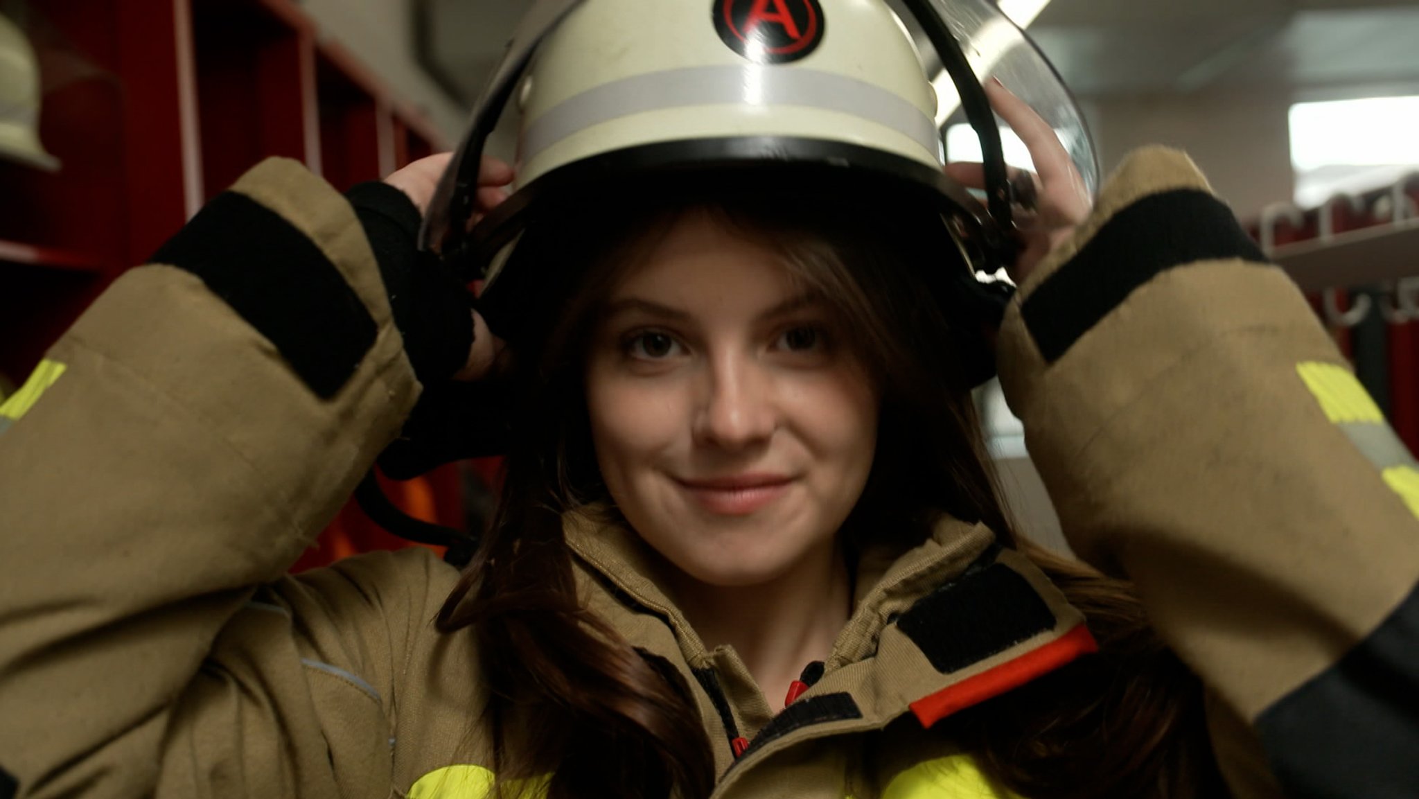 Eine Feuerwehrfrau setzt sich einen Helm auf.