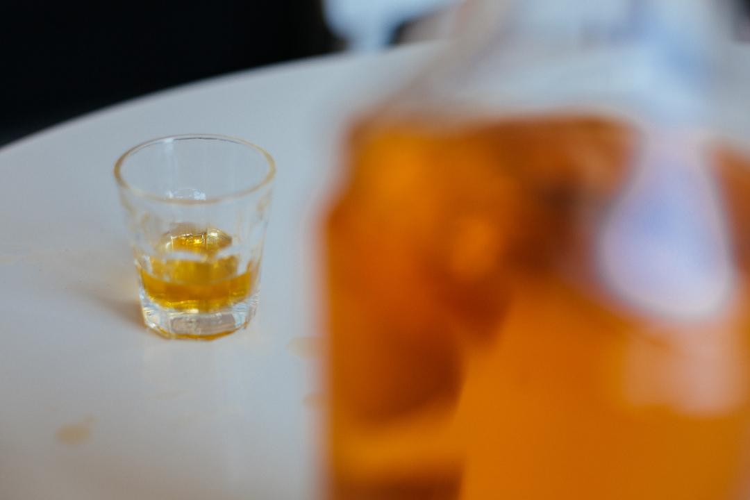 Ein Schnapsglas und eine gefüllte Flasche stehen auf einem Tisch.