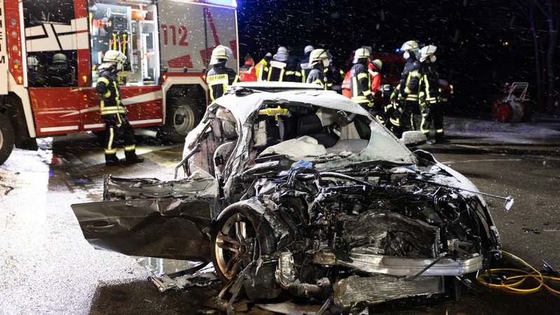 Monheim: Feuerwehrleute stehen an einer Unfallstelle hinter einem Autowrack. 