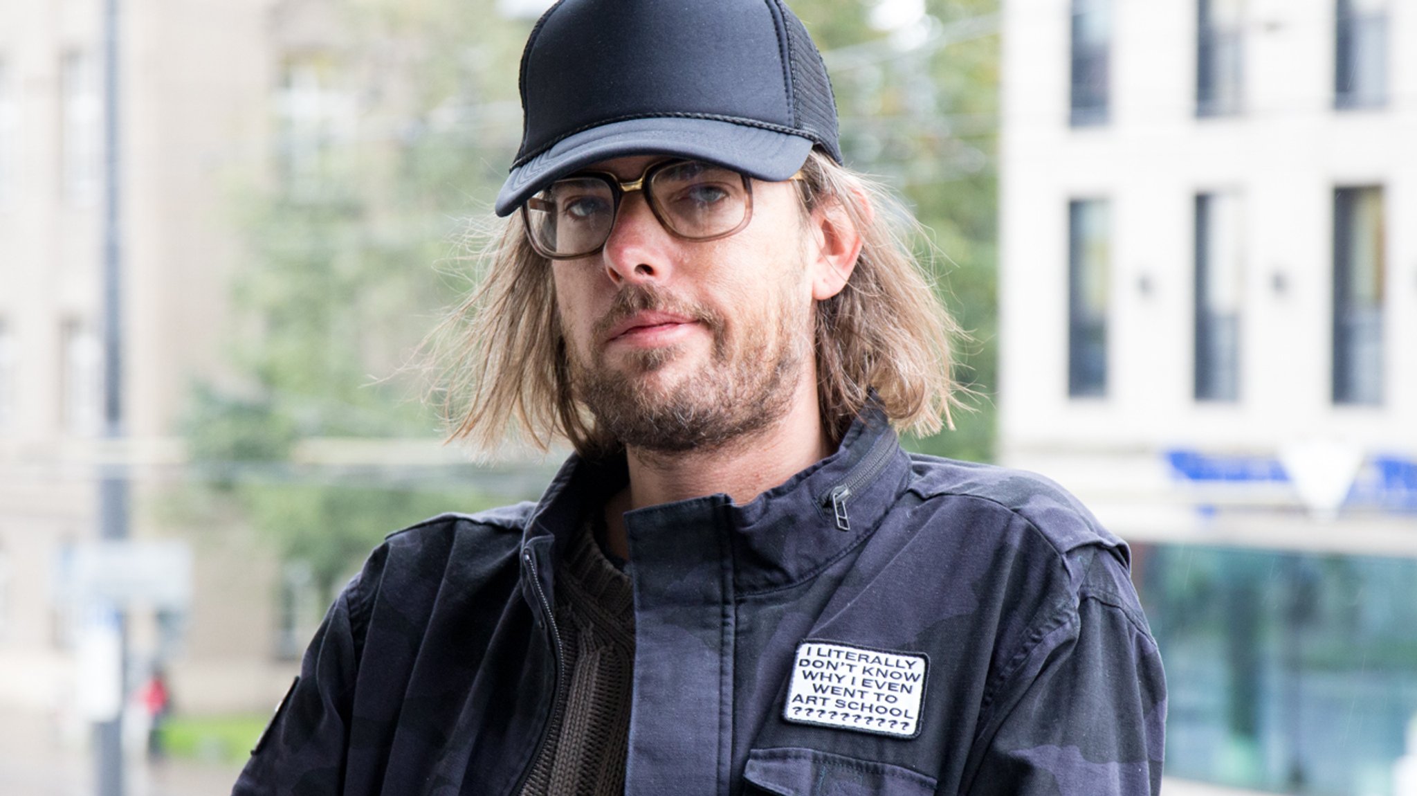 Der Münchner Musiker Sebastian Schnitzenbaumer aka BELP mit dunkelblauer Cap und dunkelblauer Jacke, darauf ein Aufnäher: "I literally don't know why I even went to art school?"