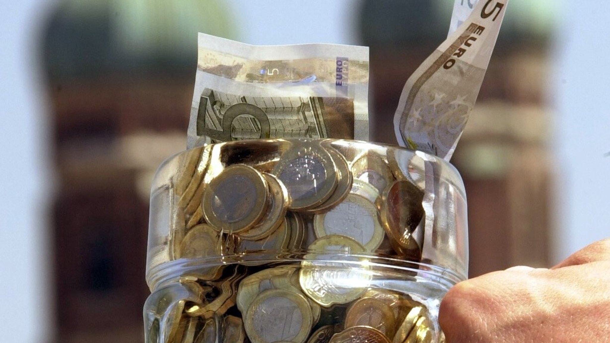 Ein Maßkrug voller Geld, dahinter die Münchner Frauenkirche.
