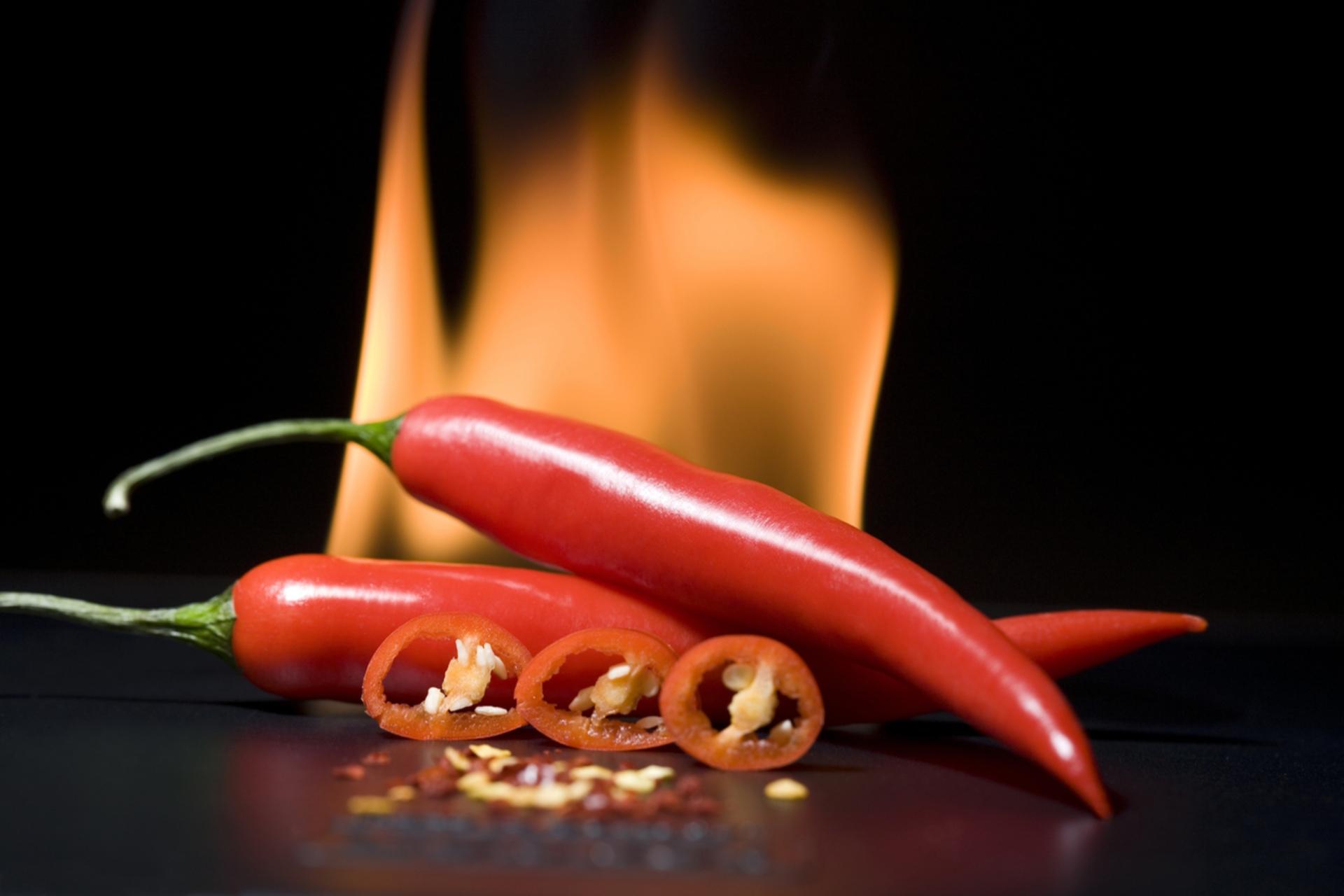 Scharfe Chilis mit Feuer im Hintergrund. Die Schärfe löst einen "Pepper-high" im Mund aus und kann süchtig machen.
