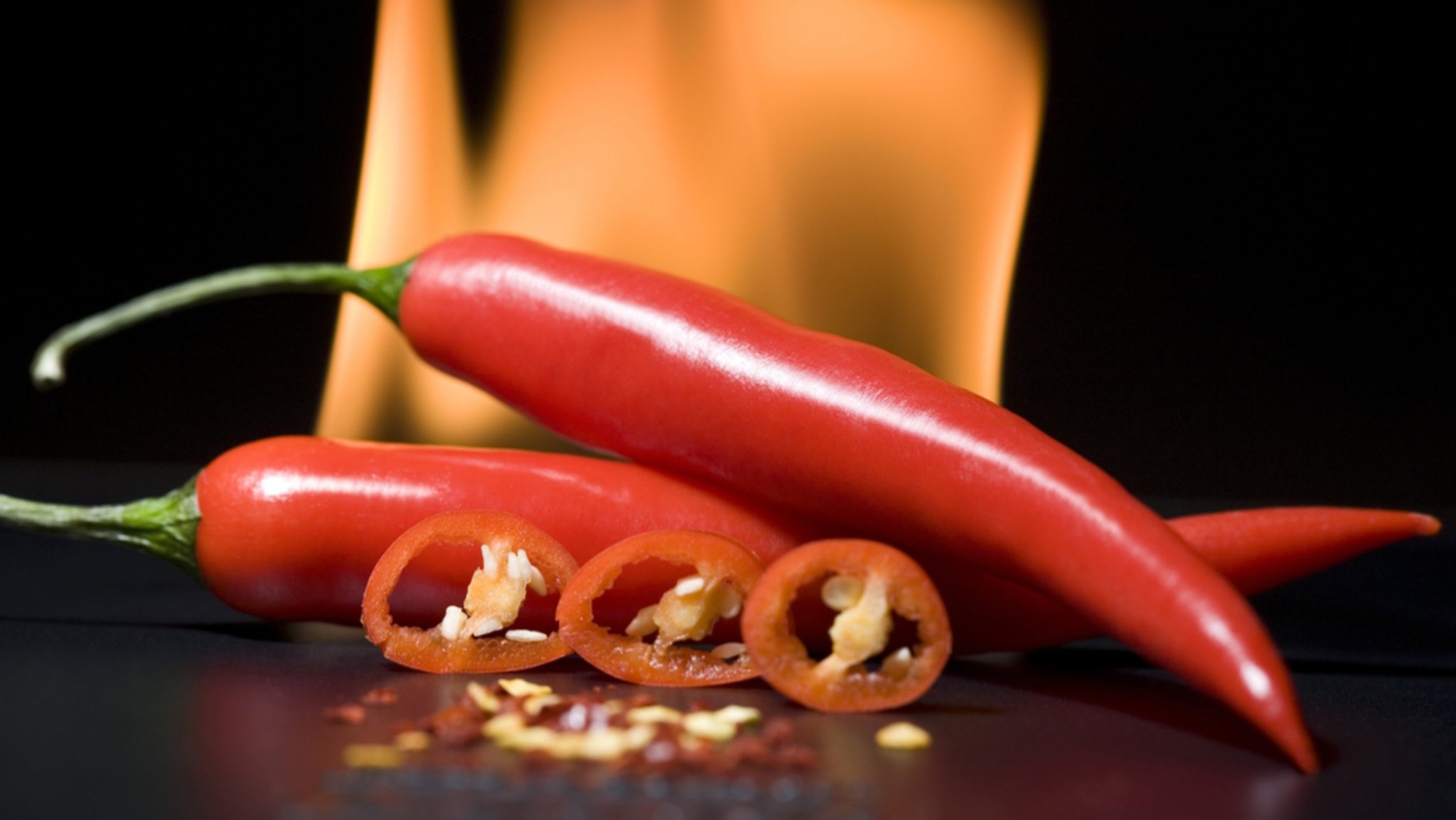 Scharfe Chilis mit Feuer im Hintergrund. Die Schärfe löst einen "Pepper-high" im Mund aus und kann süchtig machen.