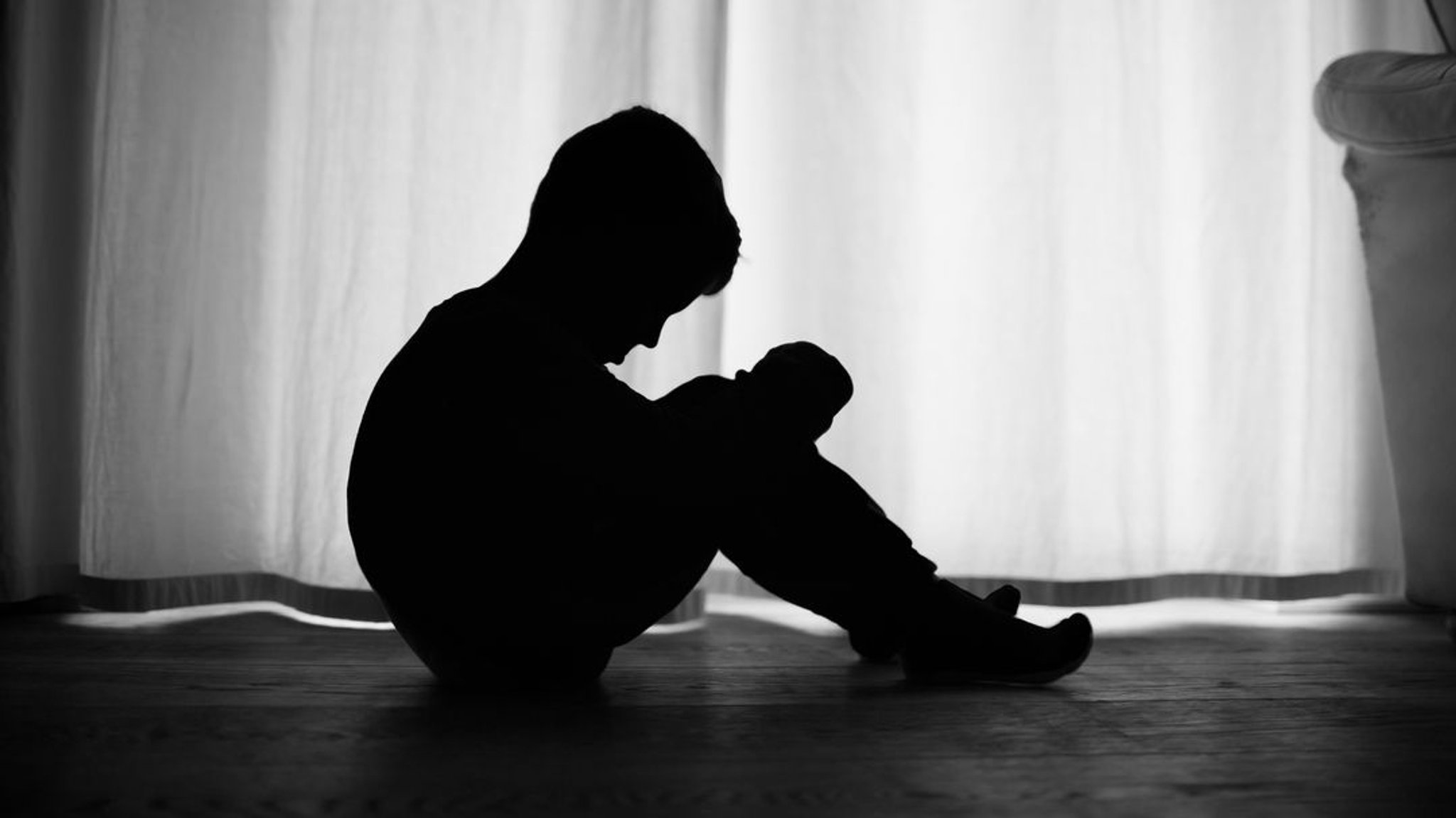 Ein Kind sitzt in seinem Zimmer vor dem Fenster und sieht traurig aus.