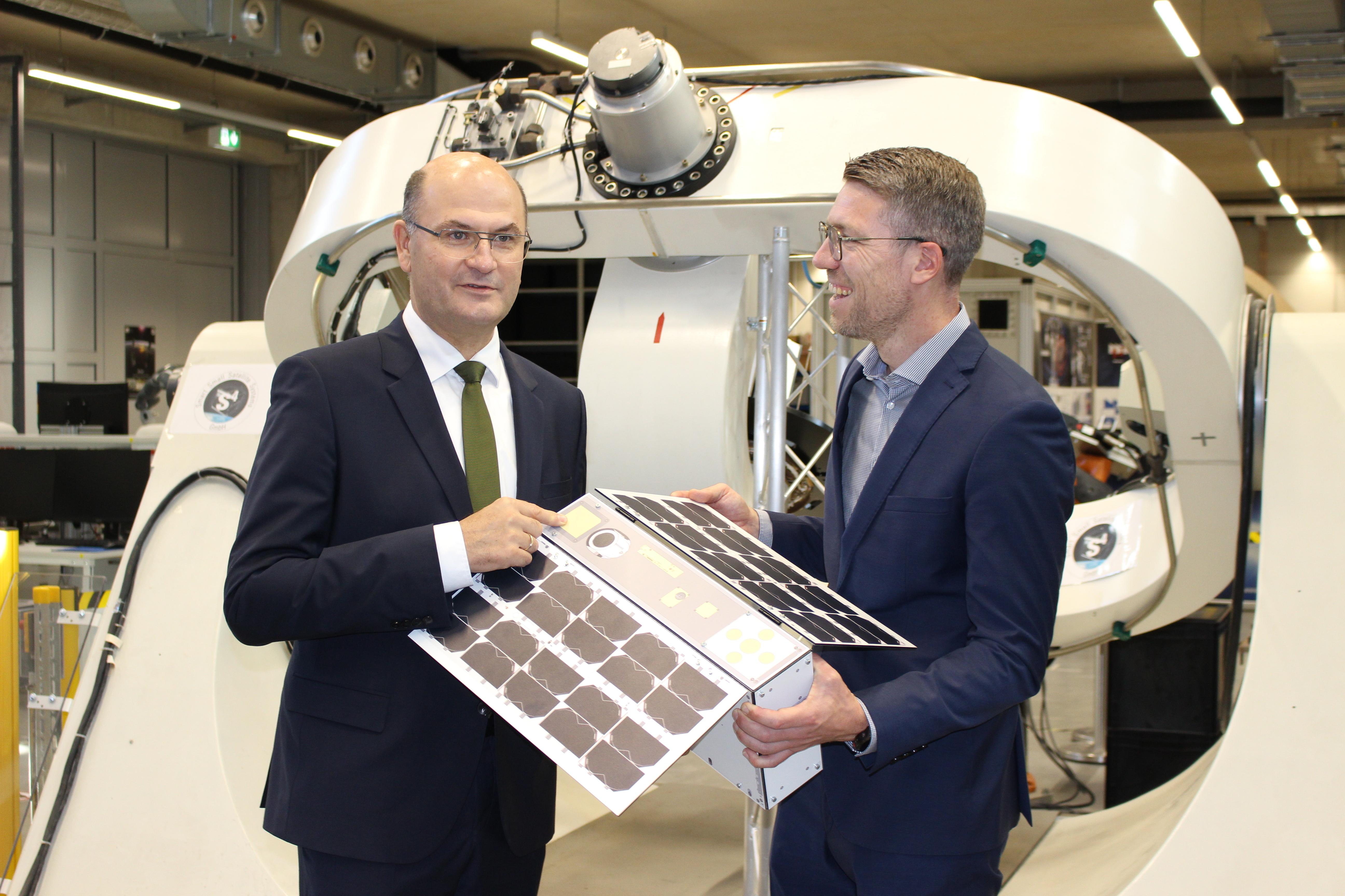 Bayerns Finanzminister Albert Füracker und Daniel Eck, Geschäftsführer des Zentrums für Telematik aus Würzburg mit dem Mini-Satelliten.