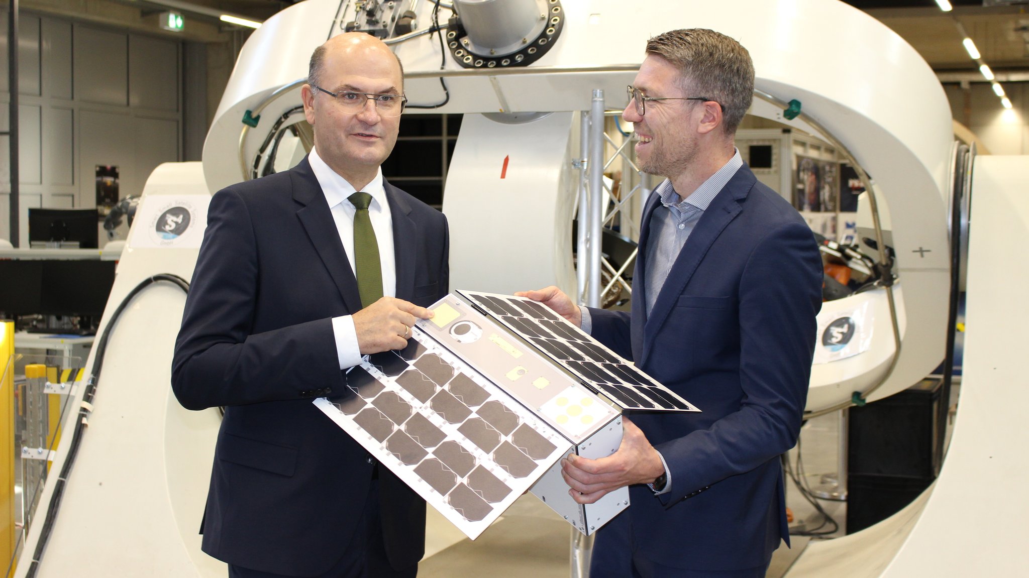 Bayerns Finanzminister Albert Füracker und Daniel Eck, Geschäftsführer des Zentrums für Telematik aus Würzburg mit dem Mini-Satelliten.